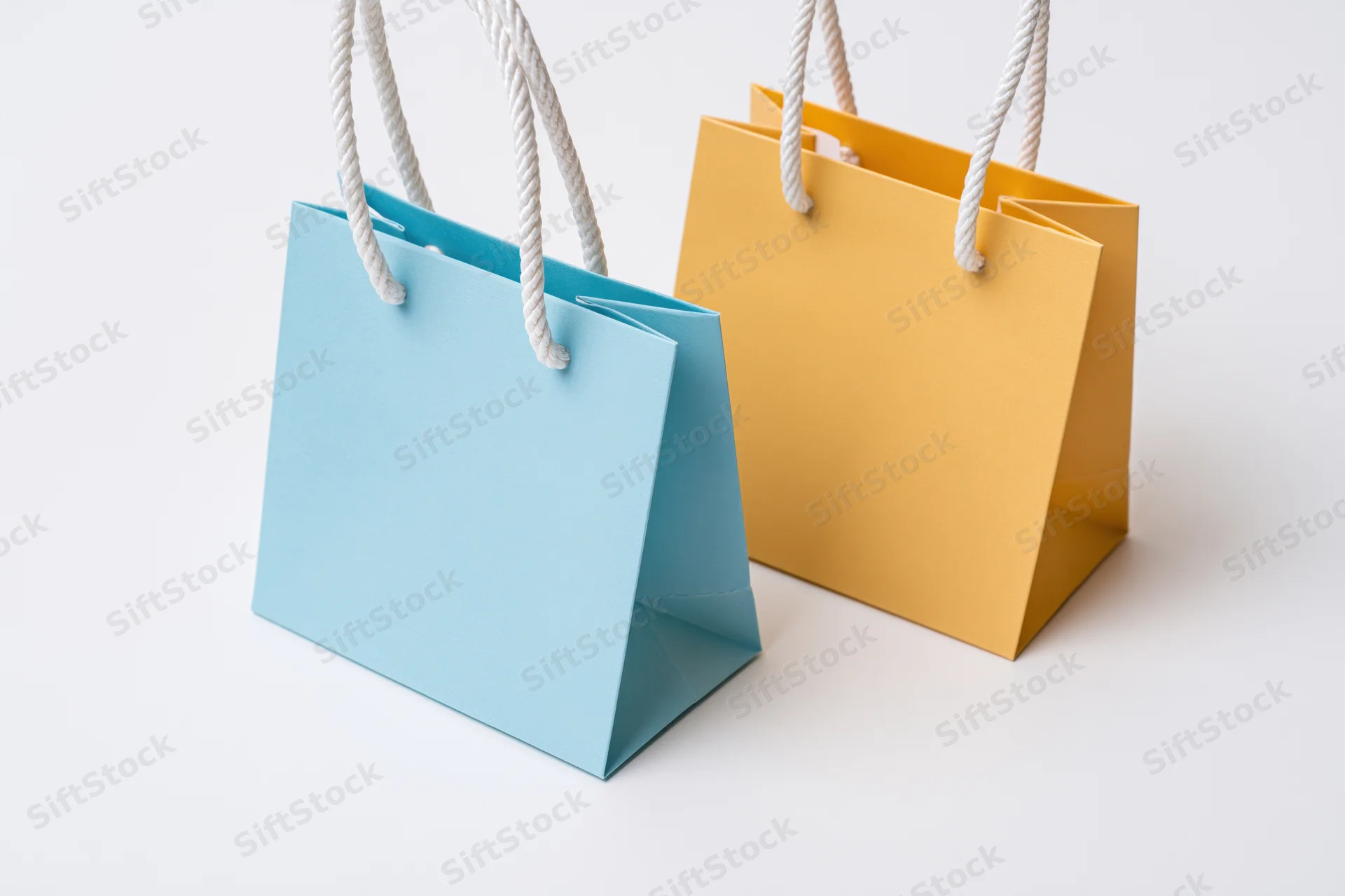 Two small paper shopping bags one light blue and one mustard on white surface