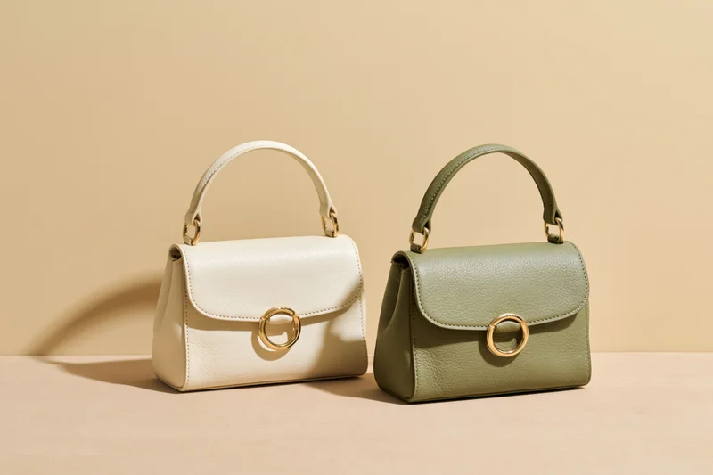 Two small structured leather handbags side by side on a smooth beige surface