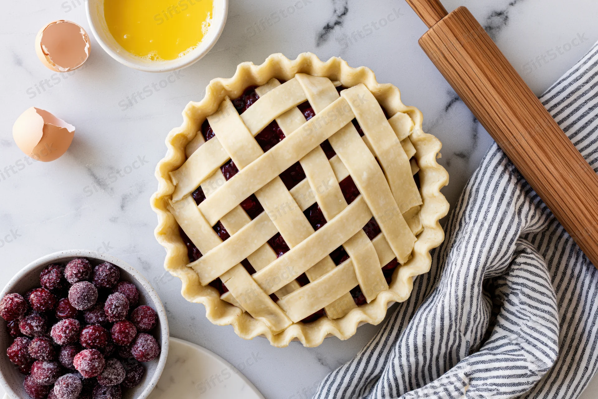 Unbaked cherry pie with lattice crust on marble countertop surrounded by baking tools and ingredients