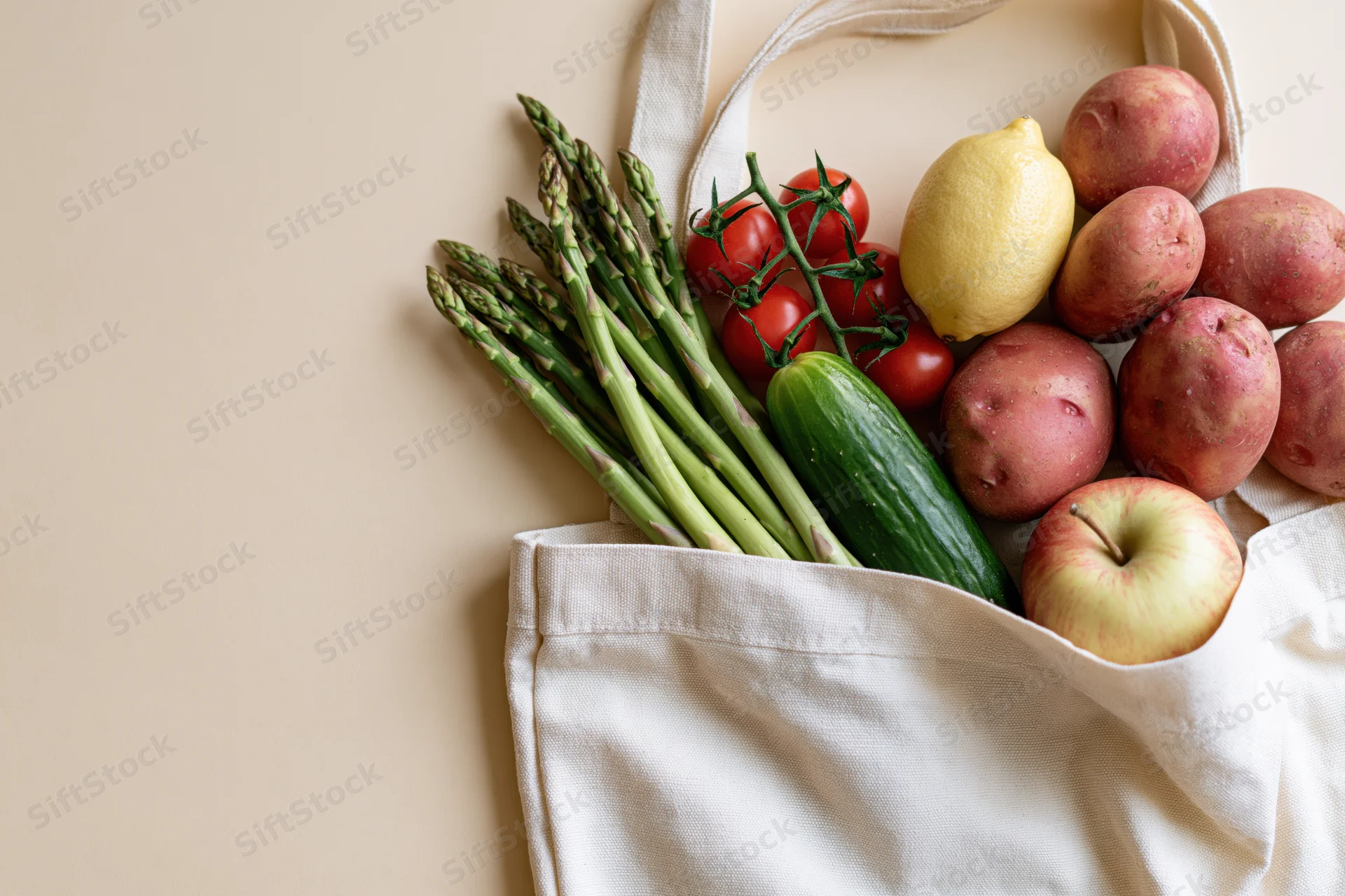 Open cotton tote bag filled with fresh vegetables and fruit on a neutral surface