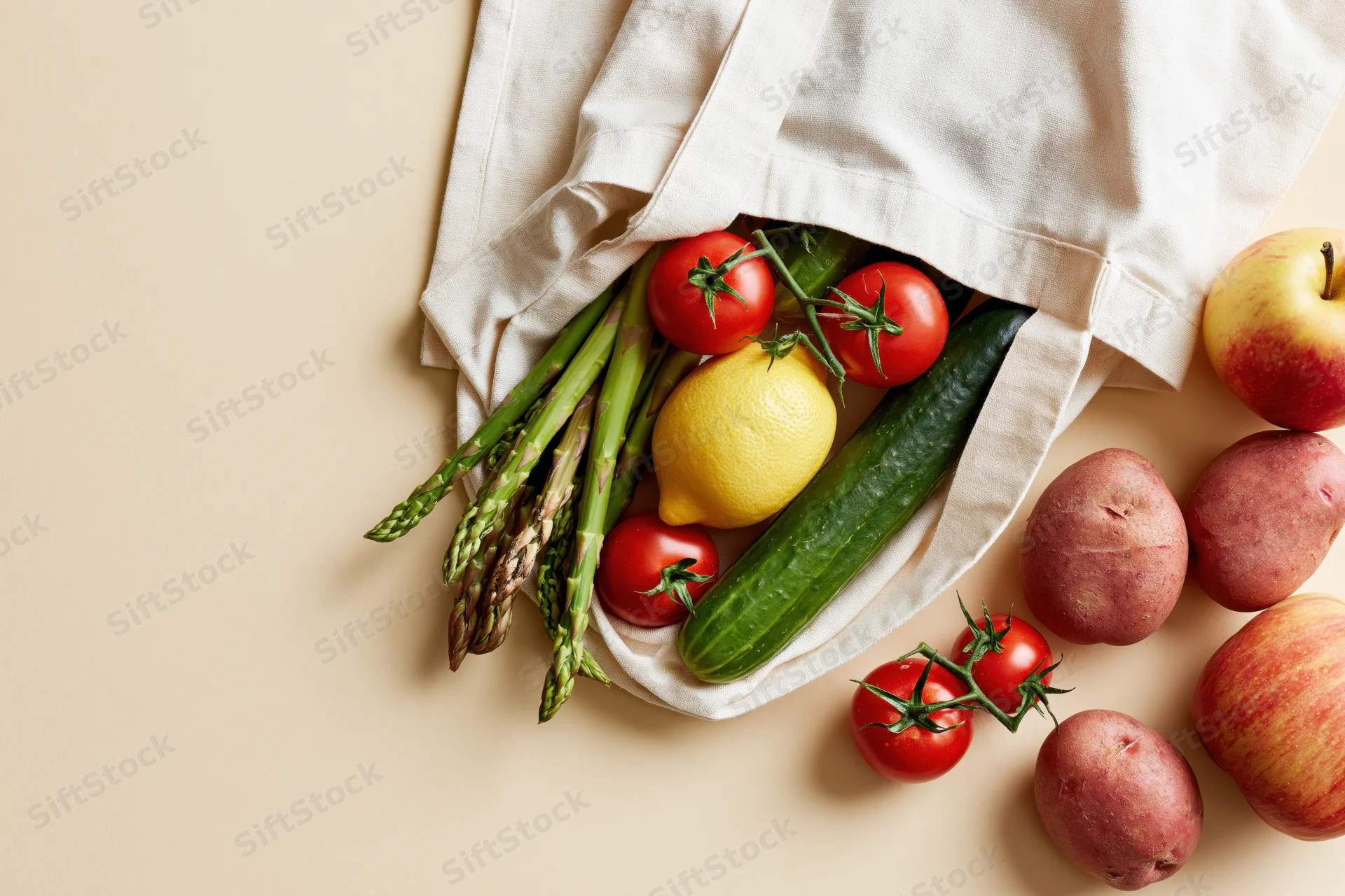 Open cotton tote bag spilling fresh vegetables and fruits onto a flat surface