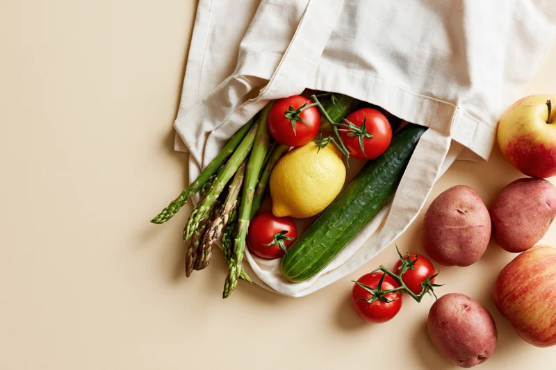 Open cotton tote bag spilling fresh vegetables and fruits onto a flat surface