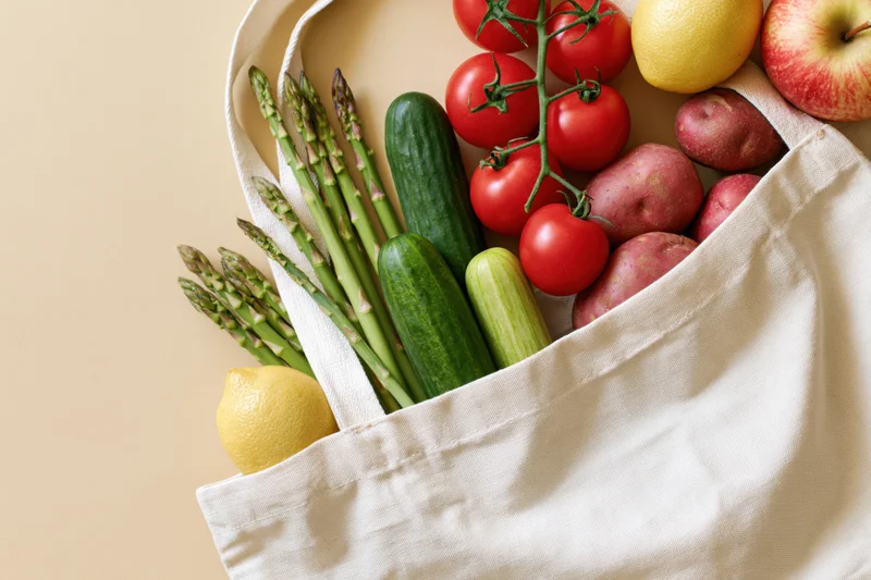 Open cotton tote bag filled with fresh vegetables and fruits on a flat surface