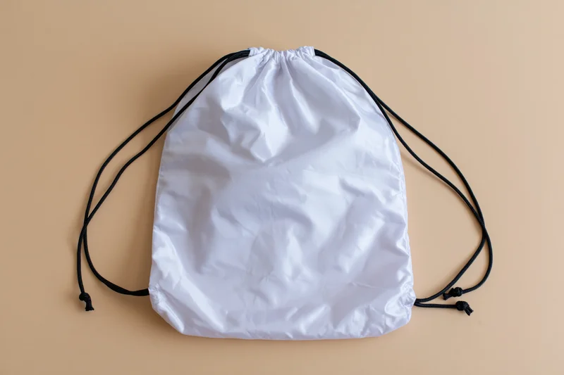 White drawstring backpack lying flat on beige surface with copyspace for branding