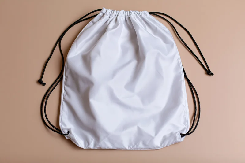 White drawstring backpack lying flat on beige surface with copyspace for design