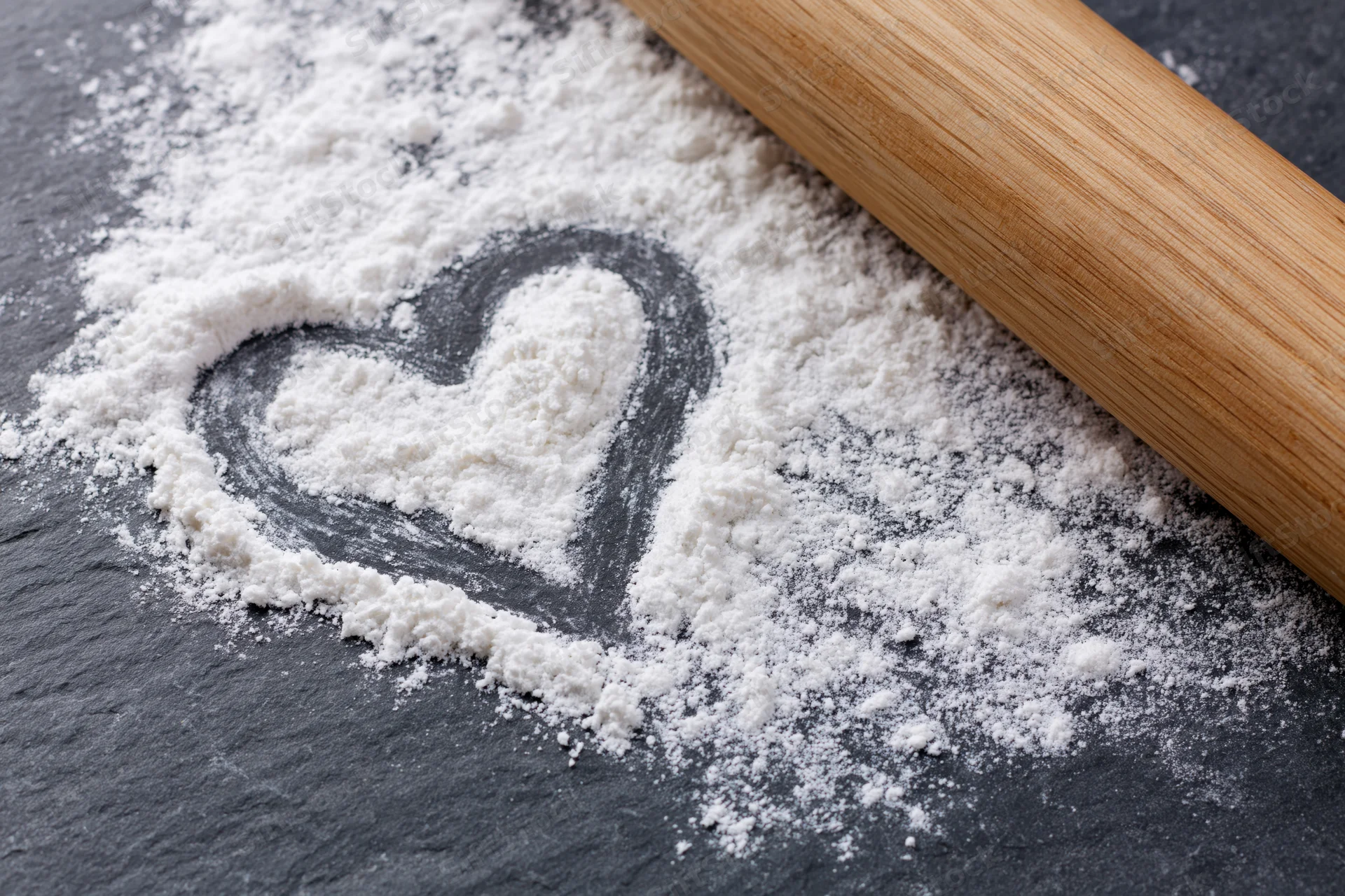 Heart shaped in flour on dark slate with wooden rolling pin beside it