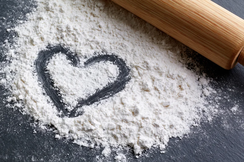 Heart shaped in white flour on dark slate surface with wooden rolling pin nearby