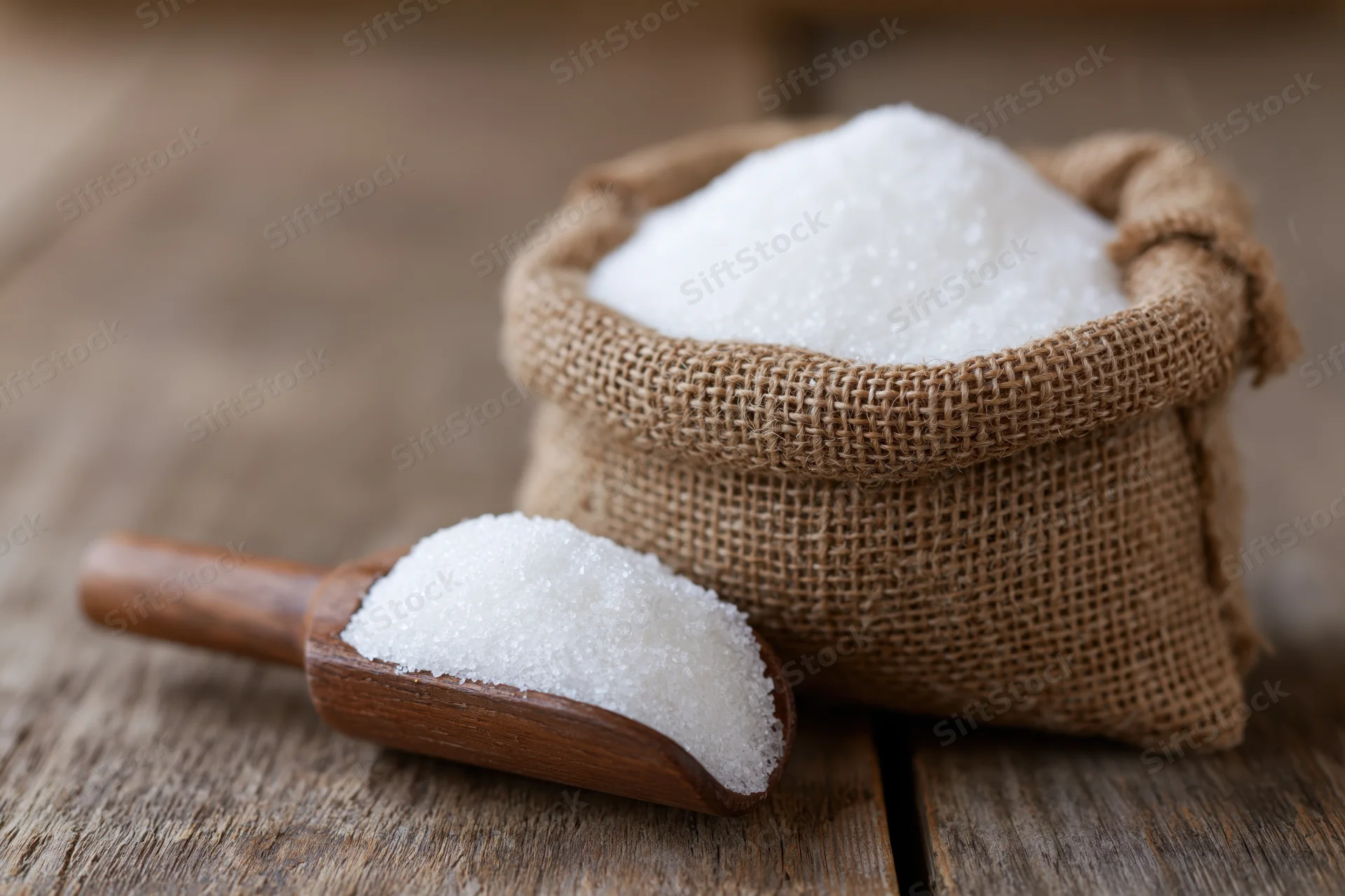 White granulated sugar in a small burlap sack with a wooden scoop on a rustic wooden table
