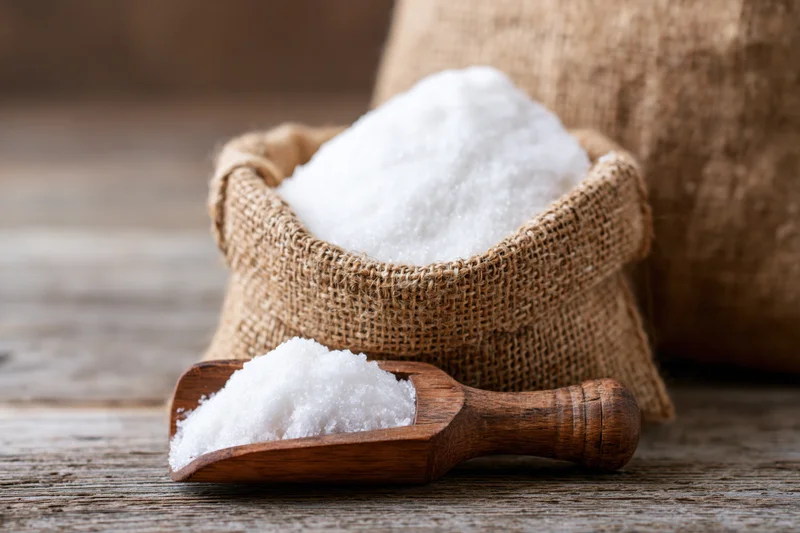 White granulated sugar in a small burlap sack with a wooden scoop on a rustic wooden table