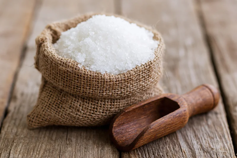 White granulated sugar in a small burlap sack with wooden scoop on rustic wooden table