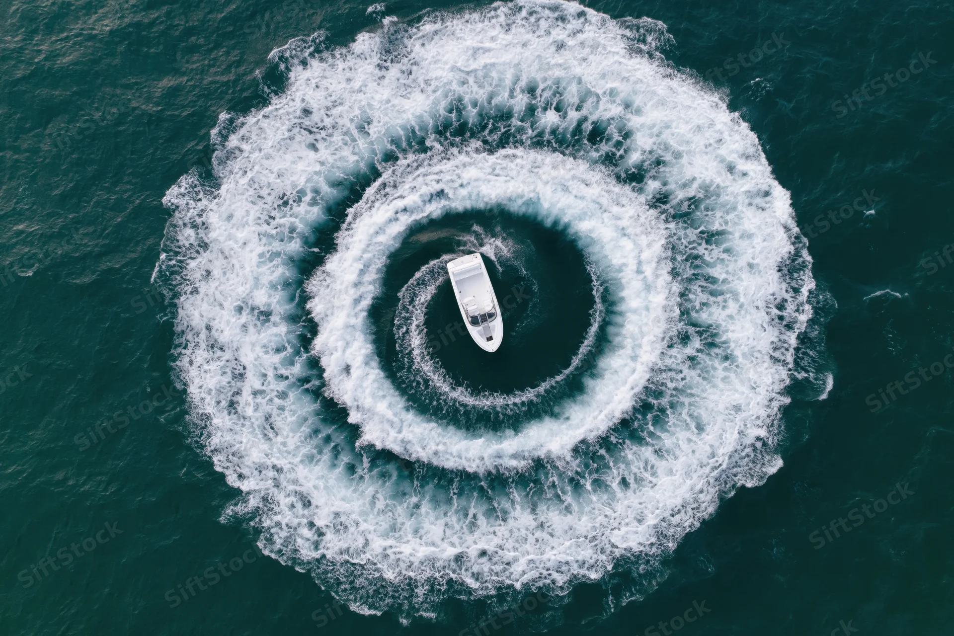 White motorboat making circular turns on open water, viewed from above