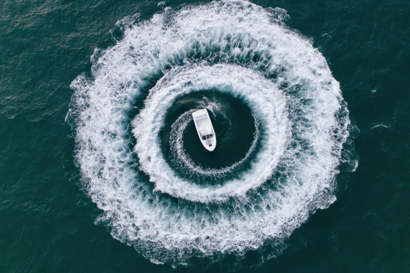 White motorboat making circular turns on open water, viewed from above