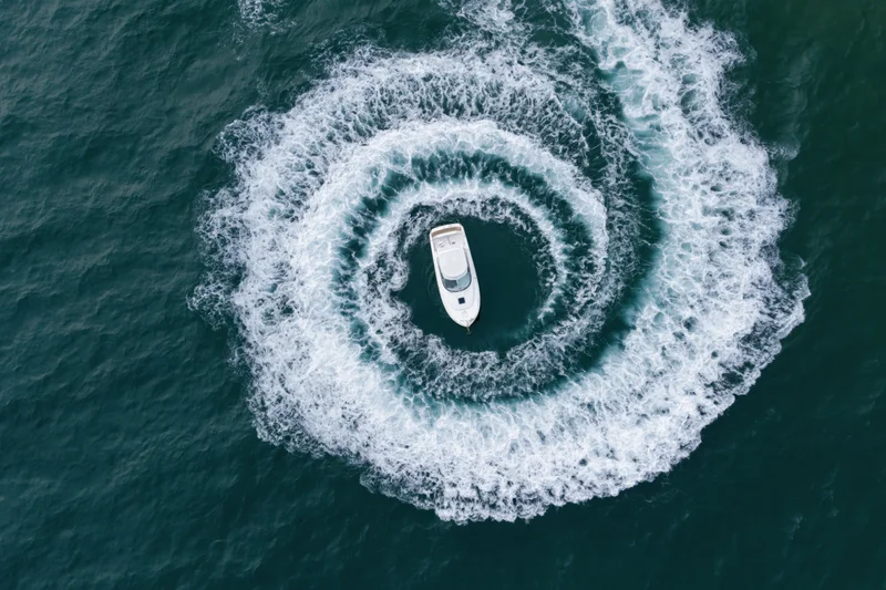 White motorboat turning in tight circular loops on open water, creating spiral wake pattern