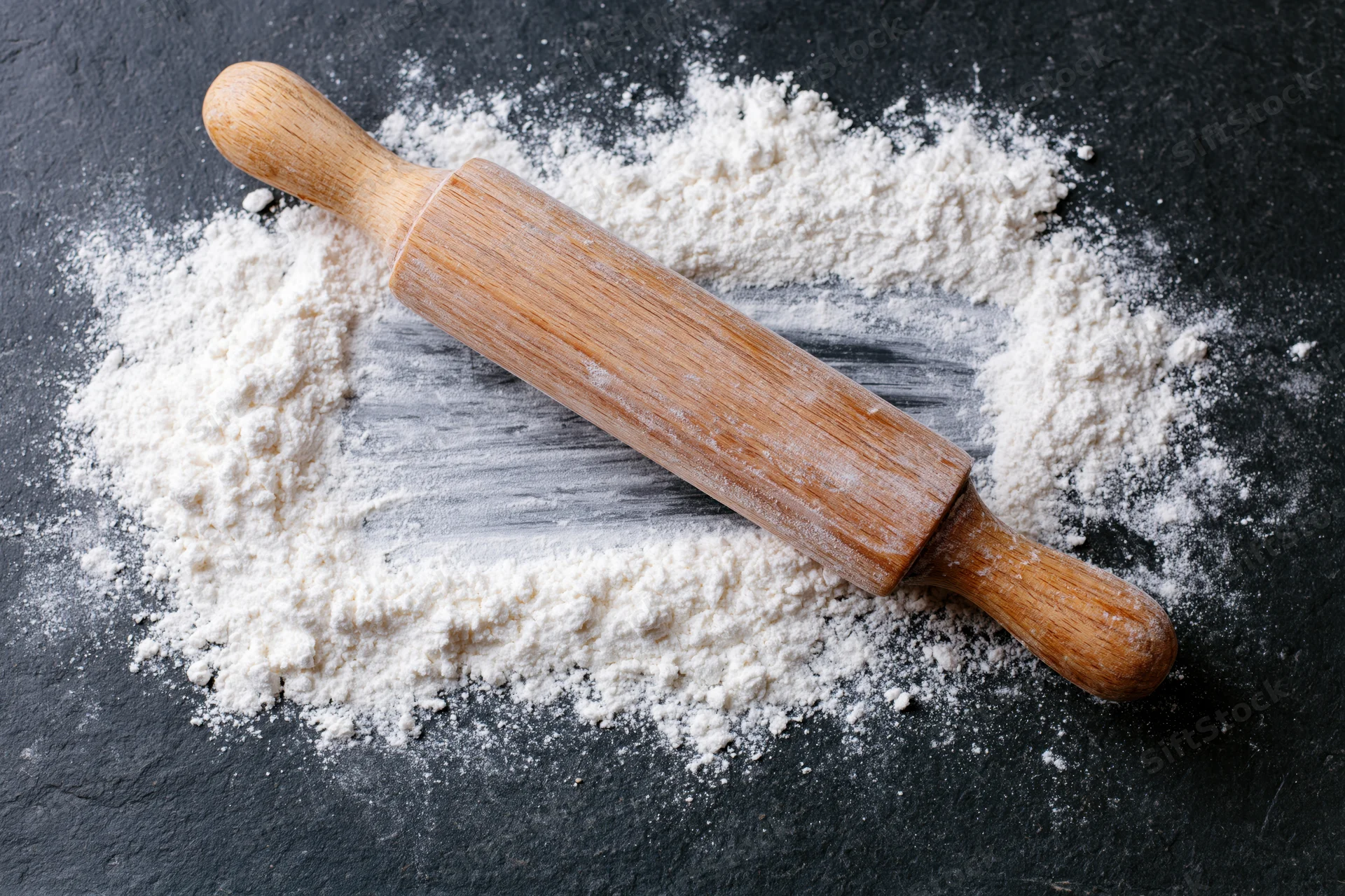 Wooden rolling pin resting on dark slate surface dusted with flour