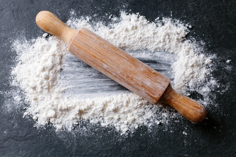 Wooden rolling pin resting on dark slate surface dusted with flour