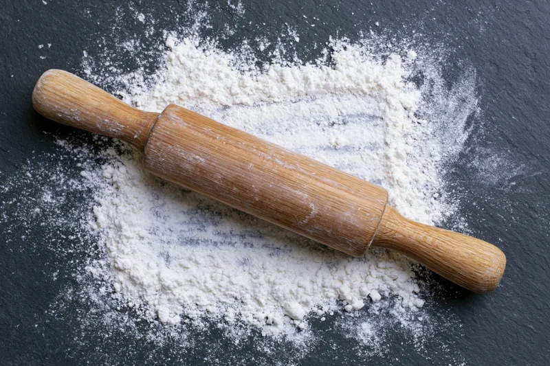 Wooden rolling pin resting on dark slate surface dusted with flour