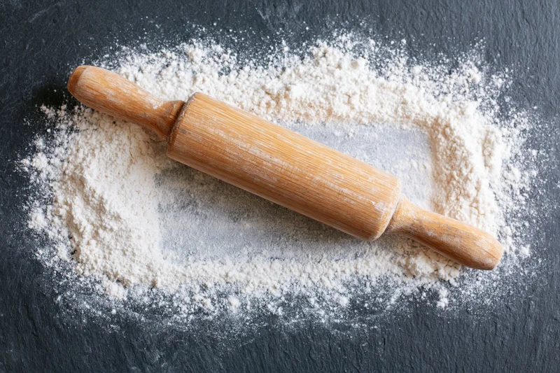 Wooden rolling pin resting on dark slate surface dusted with flour