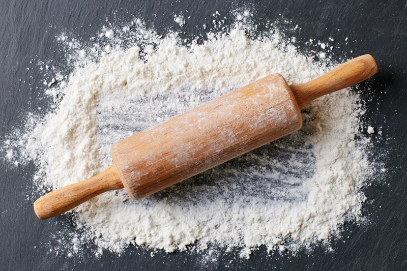 Wooden rolling pin resting on dark slate surface dusted with flour