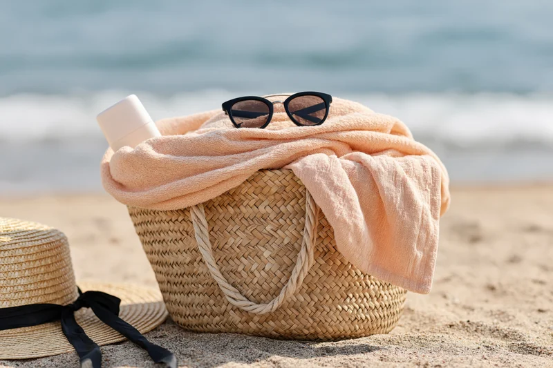 Woven straw basket with peach towel and sunglasses on sandy beach near ocean