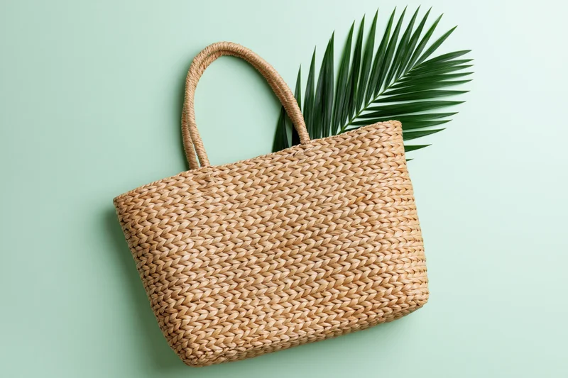 Woven straw tote bag with palm leaf on mint green background