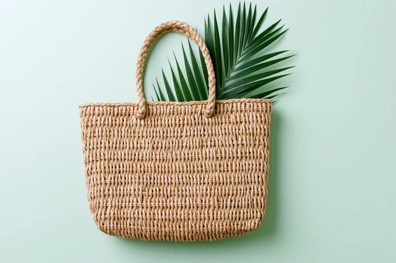 Woven straw tote bag with palm leaf on light green background