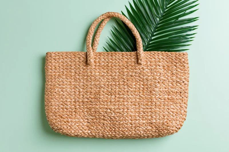 Woven straw tote bag with palm leaf on mint green background