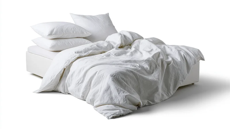 Unmade double bed with rumpled white cotton bedding and four pillows on white background