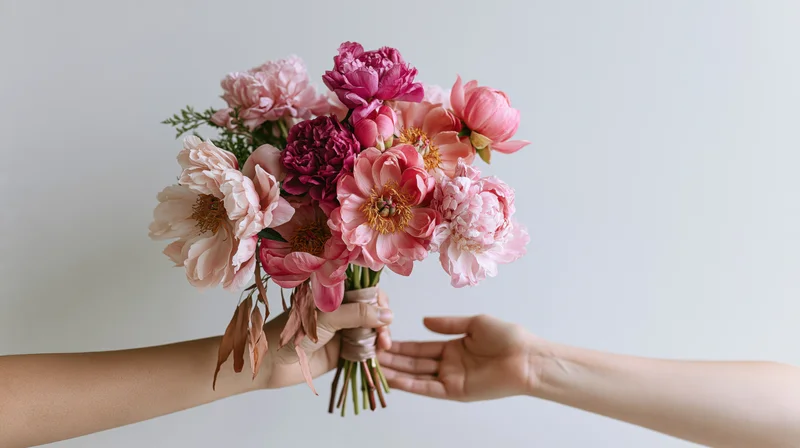 Hands exchanging a bouquet of pink peonies against a light background
