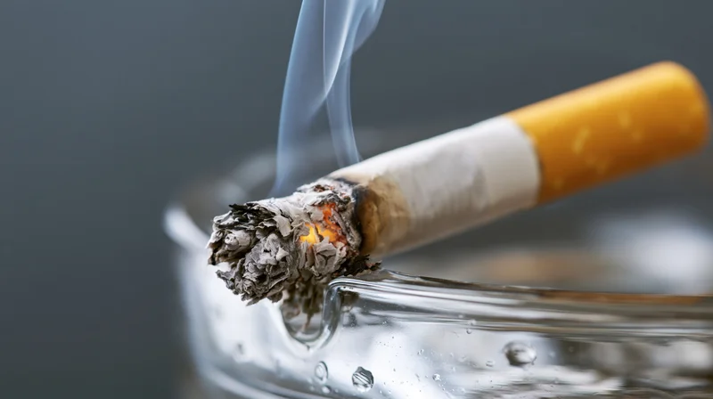 Lit cigarette with burning ember and rising smoke resting in a glass ashtray