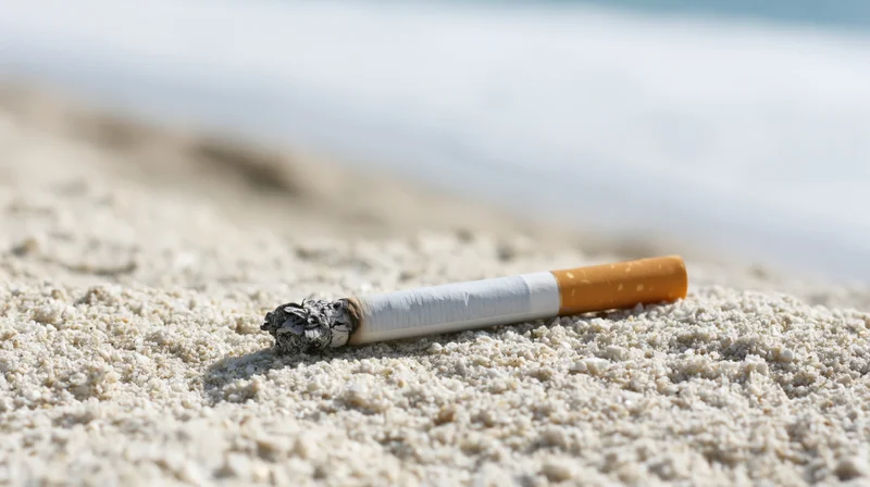 Lit cigarette lying on coarse white sand at beach with ocean in background