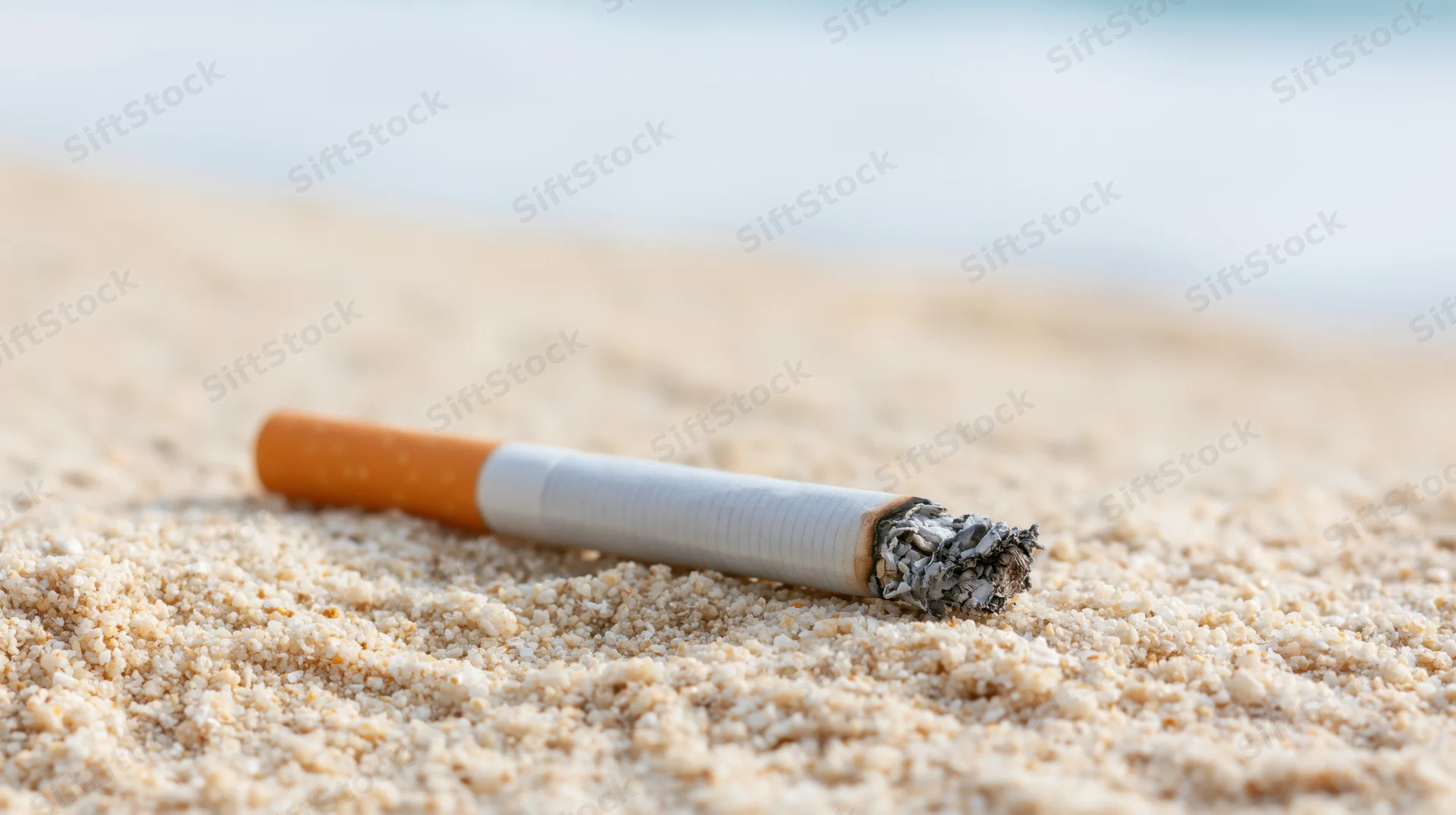 Cigarette with ash lying on coarse white sand at beach