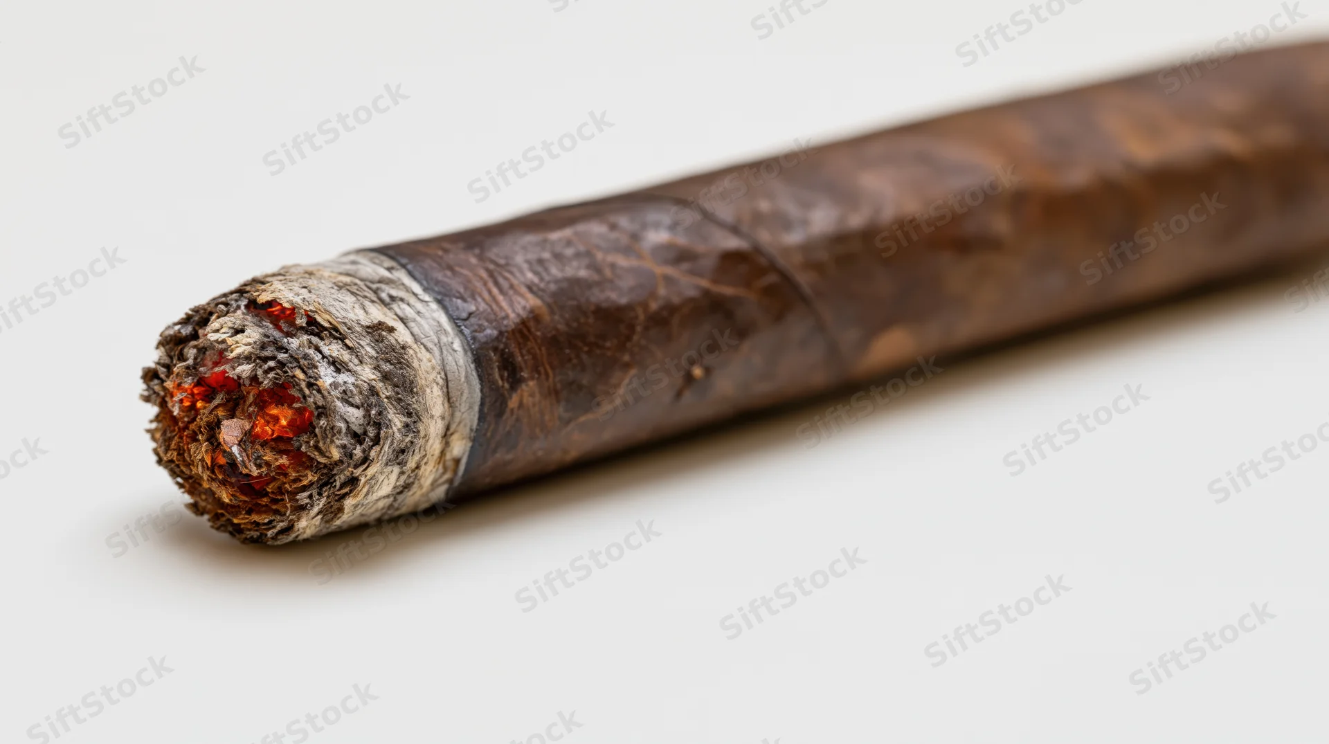 Lit premium cigar with glowing ember resting diagonally on white surface