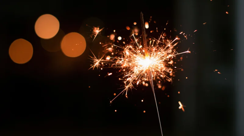 Lit sparkler burning with sparks flying outward against dark background with bokeh lights