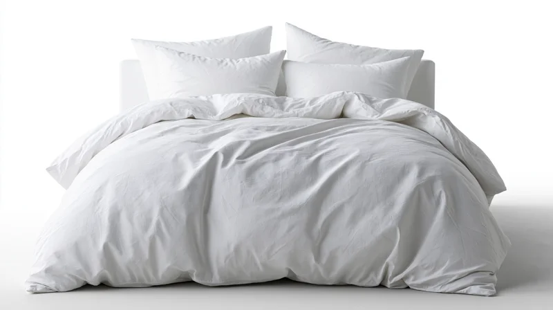 White cotton duvet and four pillows on a bed against a plain white background