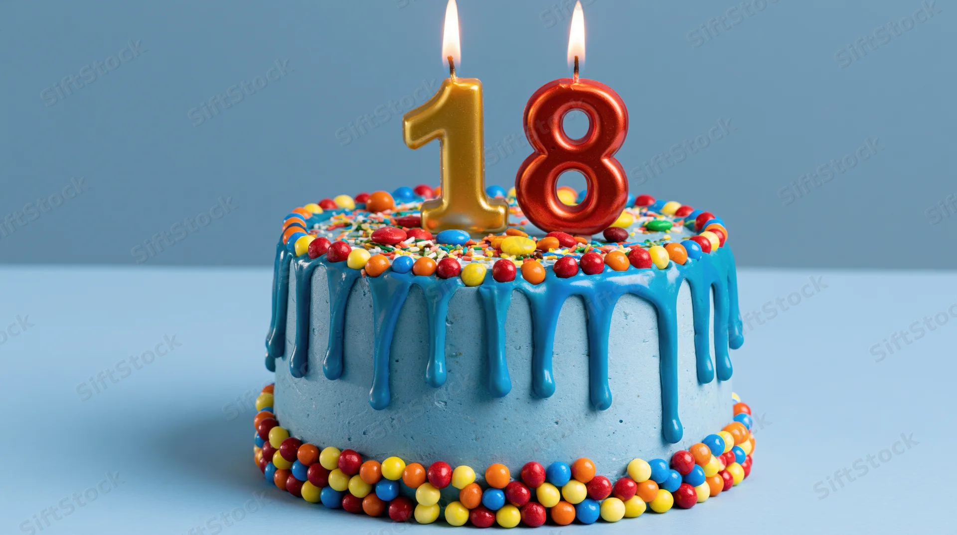 Blue frosted birthday cake with number 18 candles and colorful candy decorations on a plain surface