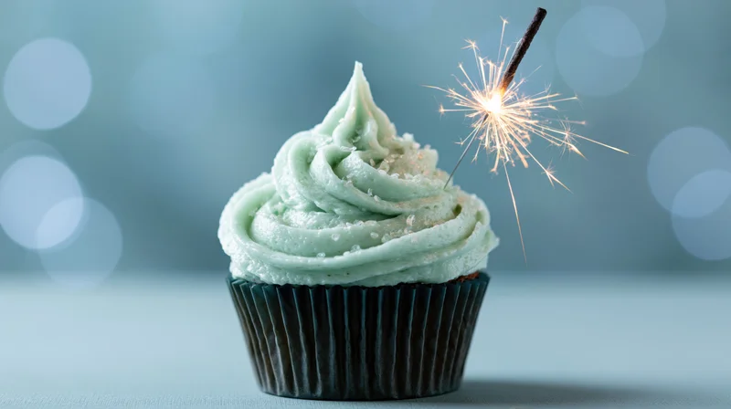 Single birthday cupcake with swirled mint frosting and lit sparkler on blue background
