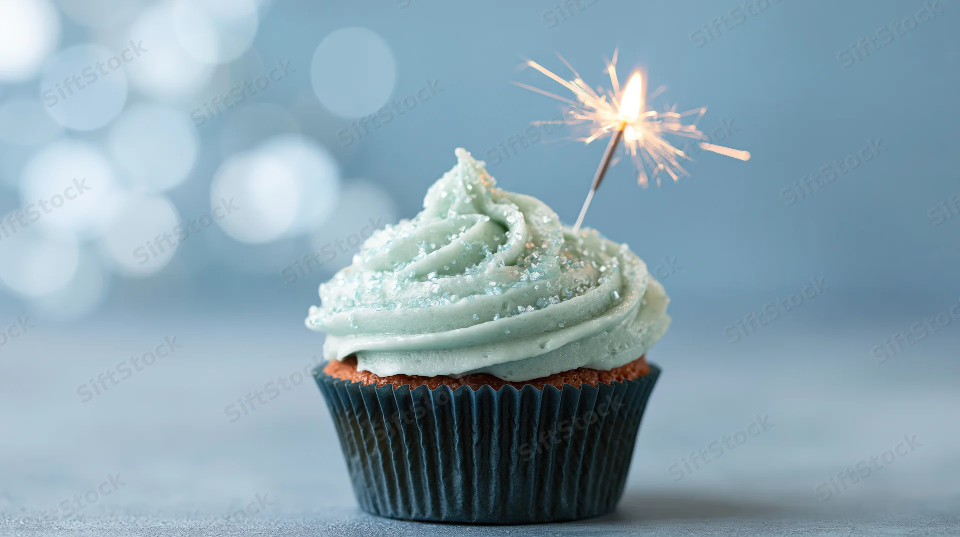 Single birthday cupcake with mint frosting and lit sparkler on blue background