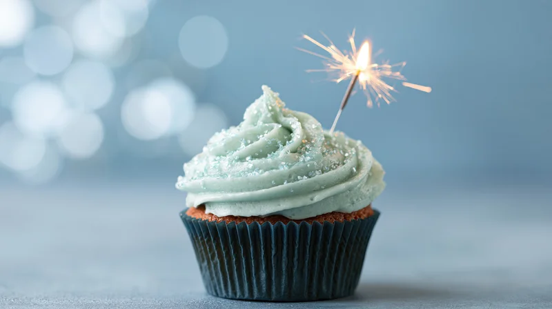 Single birthday cupcake with mint frosting and lit sparkler on blue background