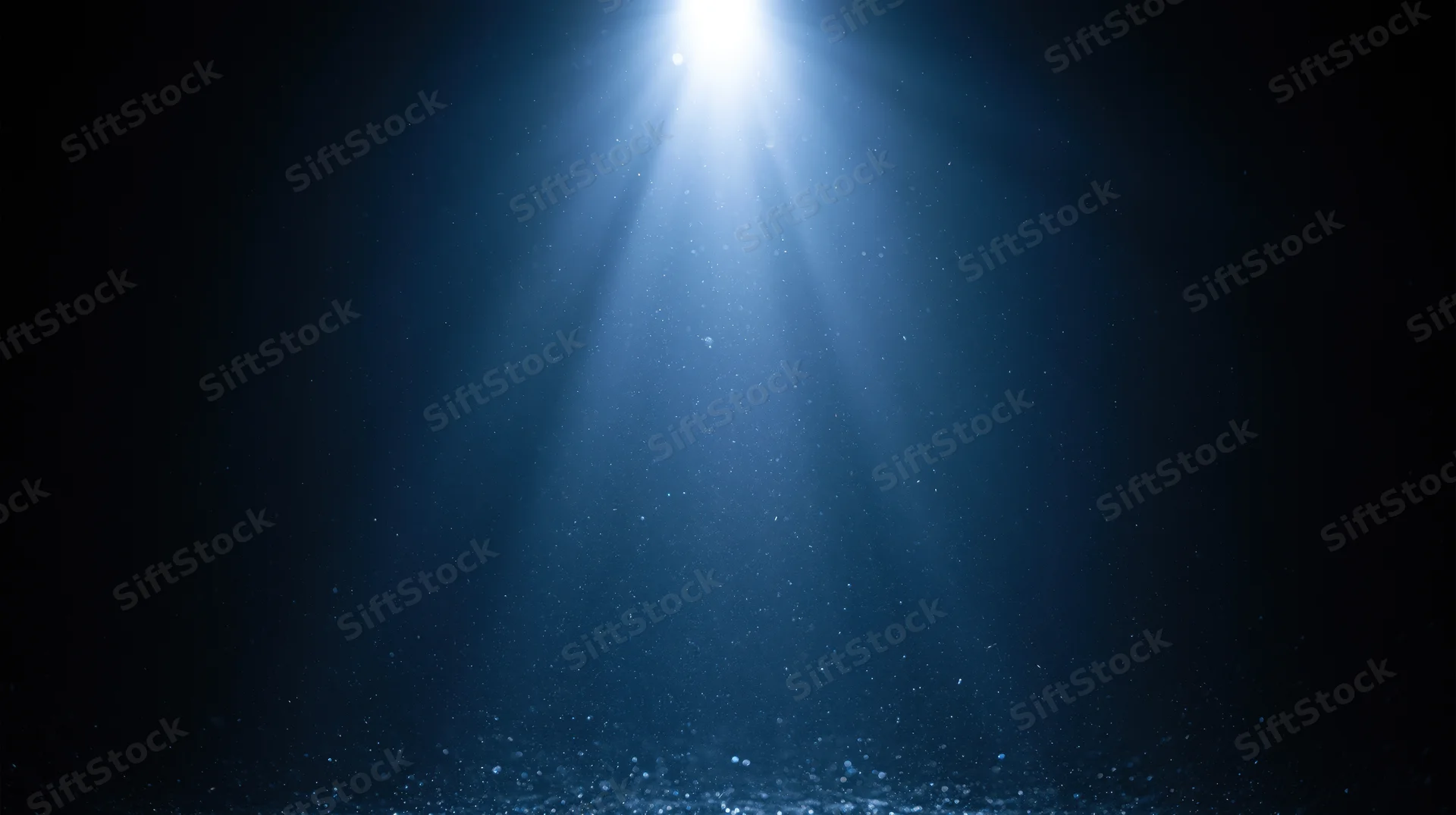 Bright spotlight beam shining downward through dark blue haze with floating particles