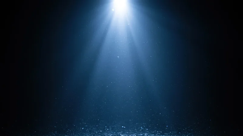 Bright spotlight beam shining downward through dark blue haze with floating particles
