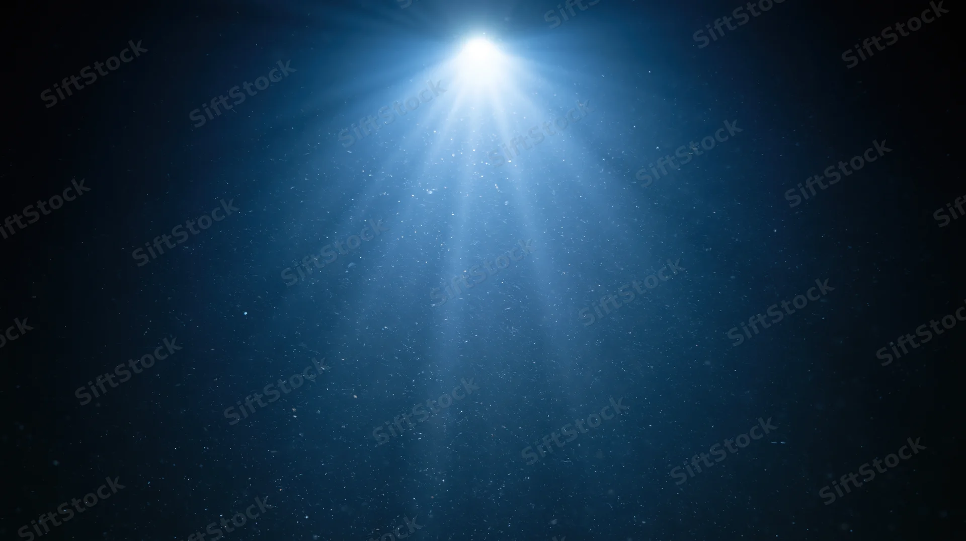 Bright spotlight beam shining down from top center through dust in dark blue space