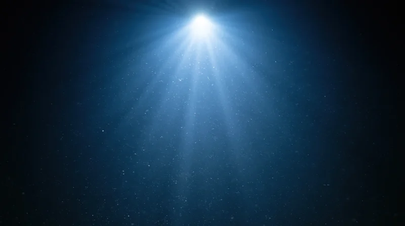 Bright spotlight beam shining down from top center through dust in dark blue space