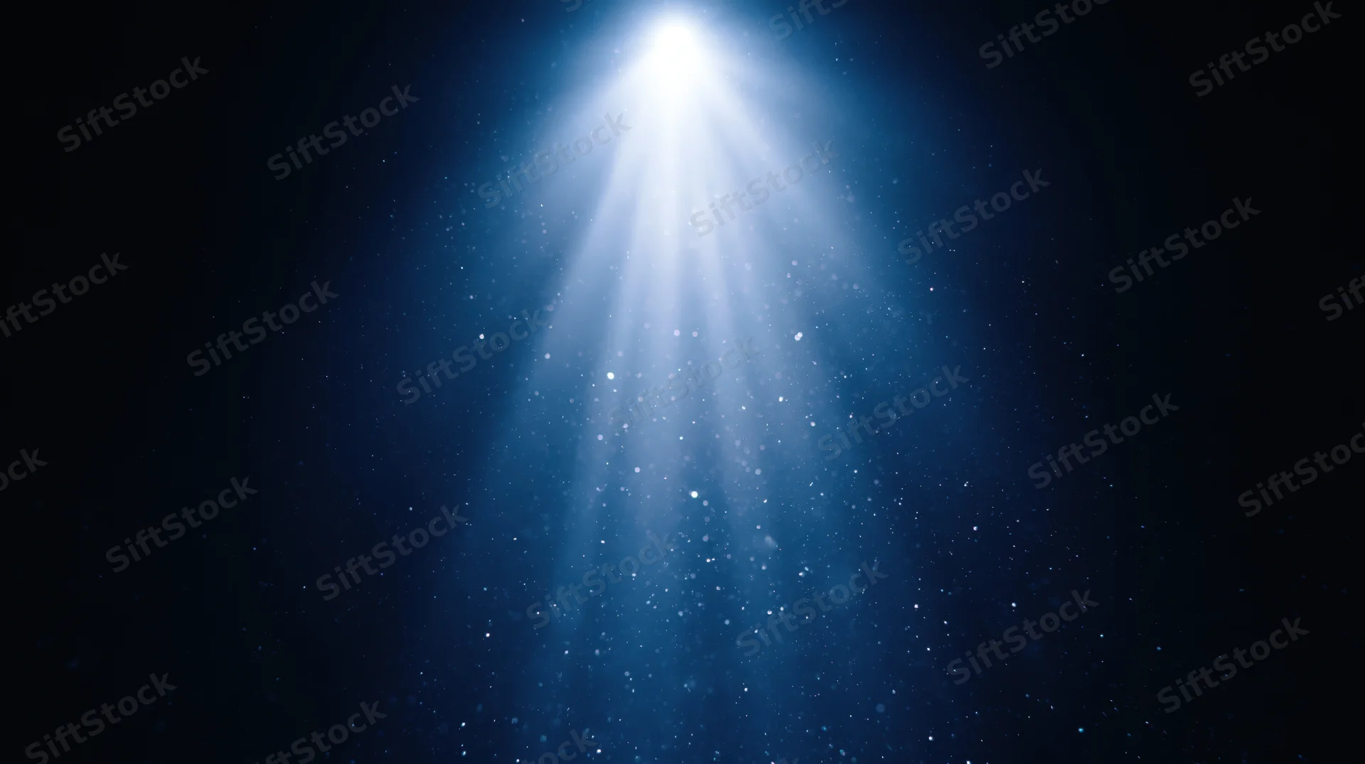 Bright spotlight beam shining downward through floating particles in dark blue space