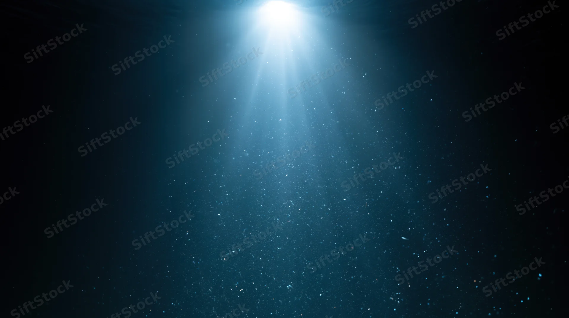 Bright light beam shining down through deep dark ocean water, illuminating floating particles