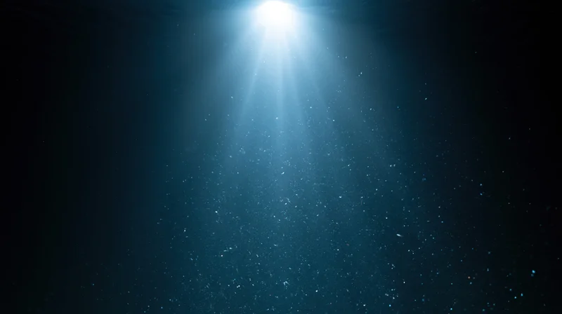 Bright light beam shining down through deep dark ocean water, illuminating floating particles