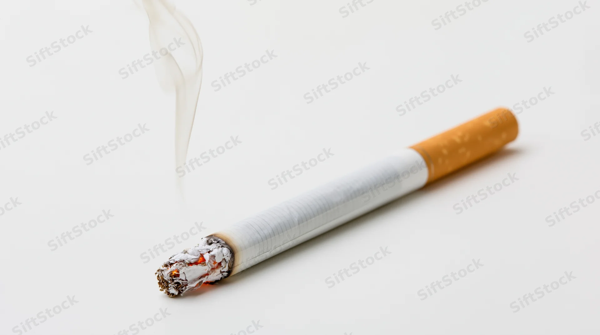 Lit cigarette burning with smoke rising, resting diagonally on white surface