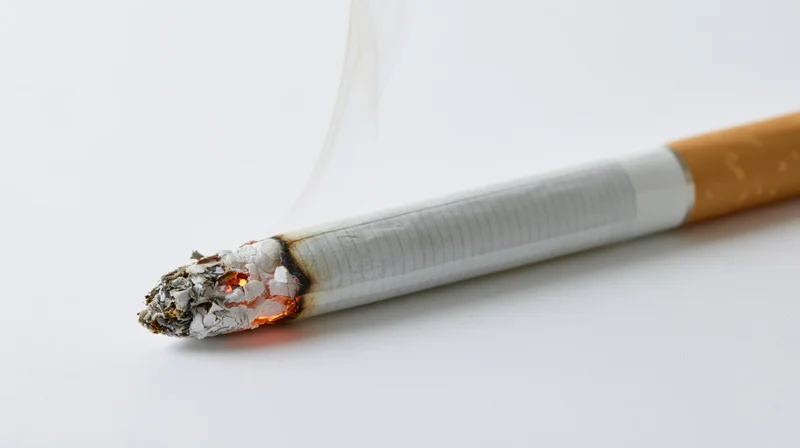 Lit cigarette burning with smoke and ash on white background