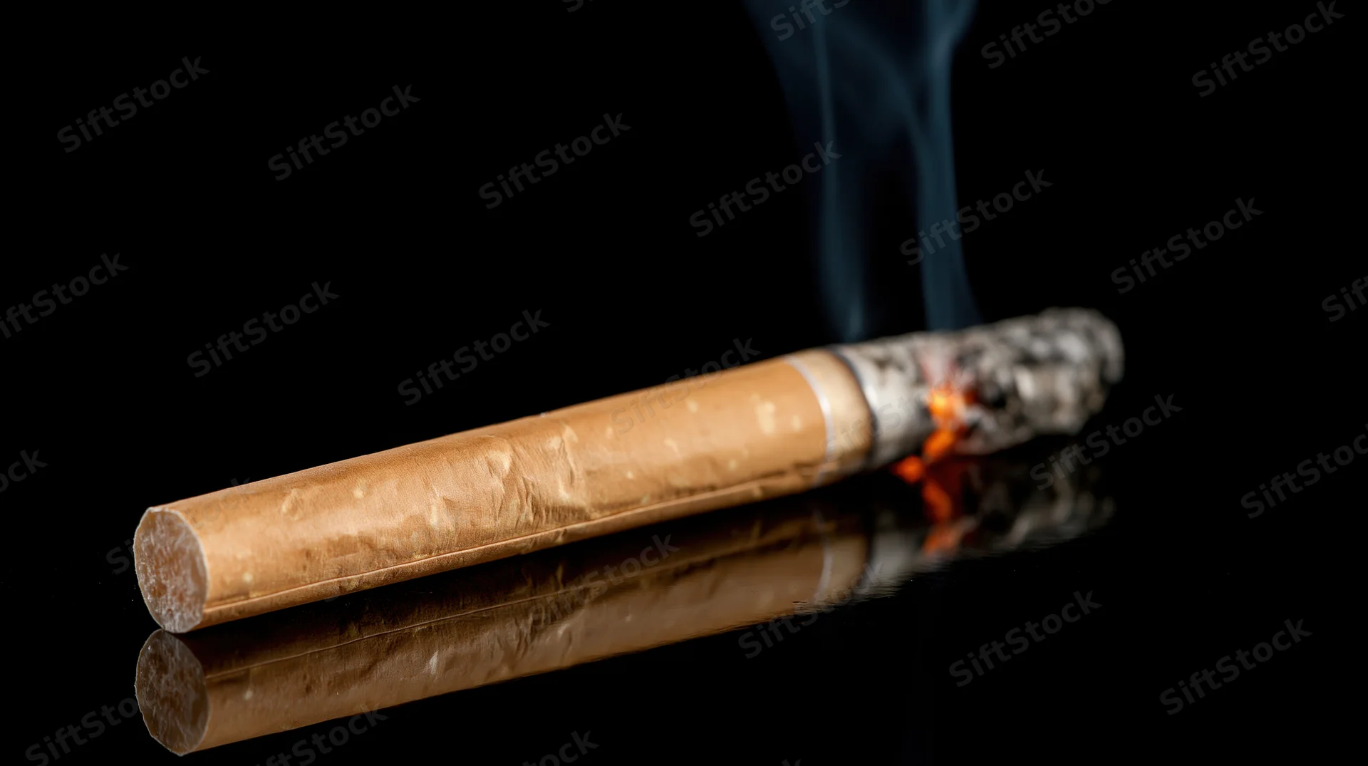Lit cigarette burning at diagonal angle on reflective black surface with smoke rising