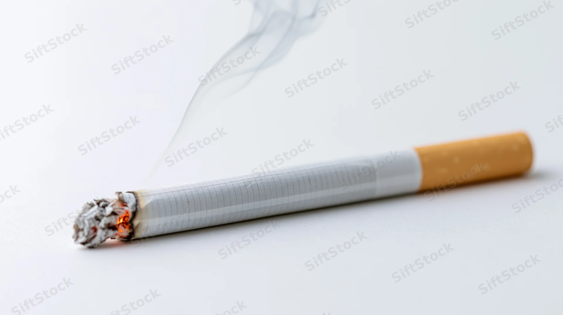 Lit cigarette with smoke and ash resting horizontally on white surface