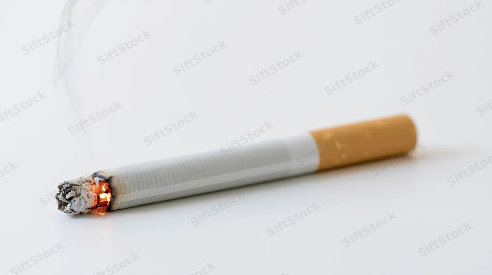 Lit cigarette burning horizontally on white surface with smoke rising